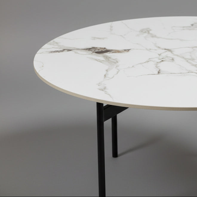 Round marble table with black legs against a brown wall