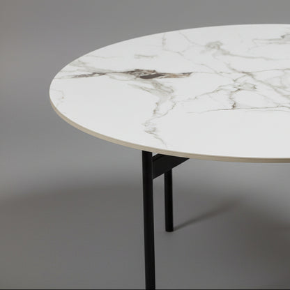 Round marble table with black legs against a brown wall